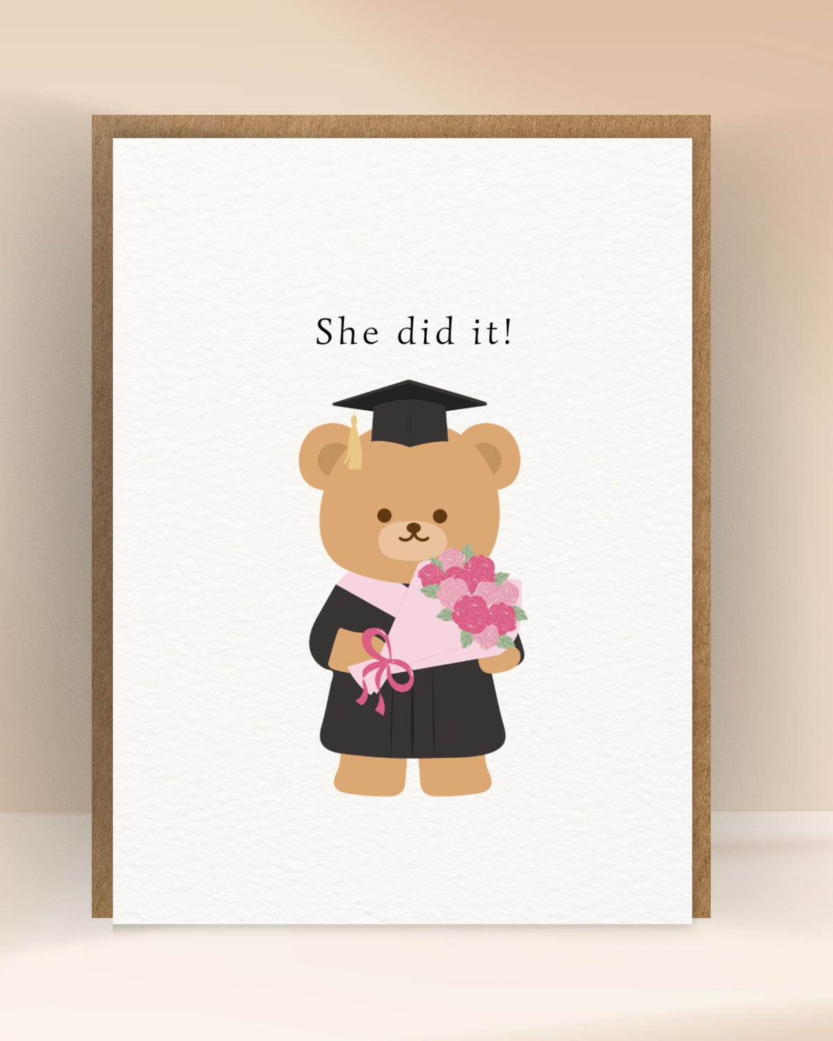 Afstudeerkaart met de tekst ‘She did it!’ en een beer in toga met een boeket roze bloemen